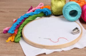 The embroidery hoop with canvas and bright sewing threads for embroidery in - The Creative Folk Embroidery hoop with white fabric, skeins of colorful floss and a thimble