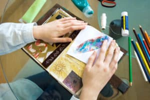 Best Scrapbook Kits - The Creative Folk Hands assembling a scrapbook page with patterned paper and pencils