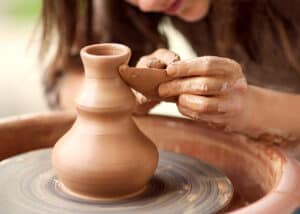 The Absolute Best Gifts for Potters - The Creative Folk Hands shaping a clay vase on a spinning pottery wheel