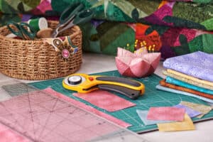 Best Pressing Mats For Quilting - The Creative Folk Rotary cutter, pins and folded quilting fabrics on a green cutting mat