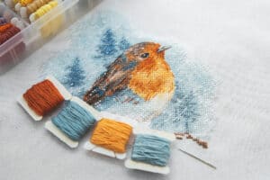 Frogging In Cross Stitching - The Creative Folk Cross stitch project in progress with floss bobbins and a needle on white canvas