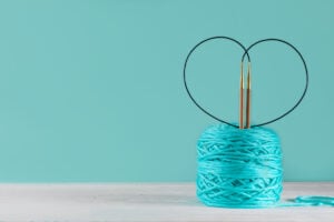 Best Circular Knitting Needles For Socks - The Creative Folk Ball of turquoise yarn with circular knitting needles curved into a heart