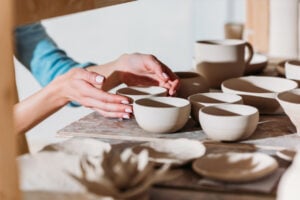 Ceramics Vs Pottery - The Creative Folk Hands arranging unfired white ceramic bowls on a board