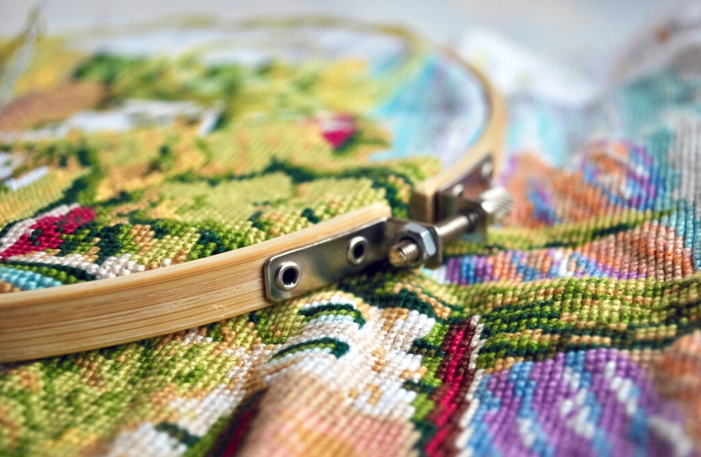 Alternatives To Framing Cross Stitch - The Creative Folk Finished cross stitch piece held in a wooden hoop beside floss and scissors
